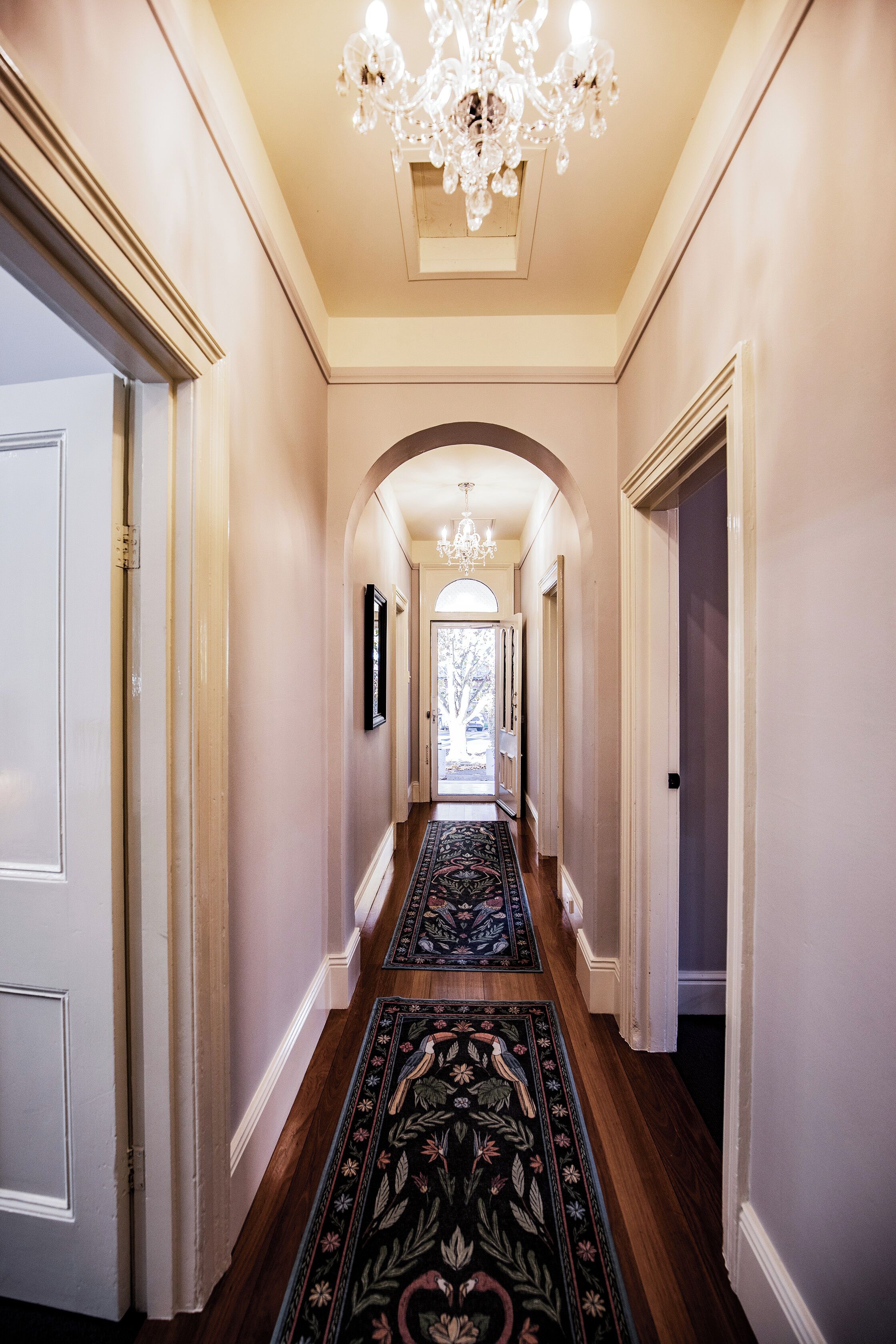 Un couloir agrémenté d’un lustre, d’un parquet en bois et d’un tapis à motifs.