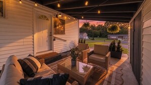 Een overdekt terras met rieten meubilair, een glazen tafel en hangende lampen.
