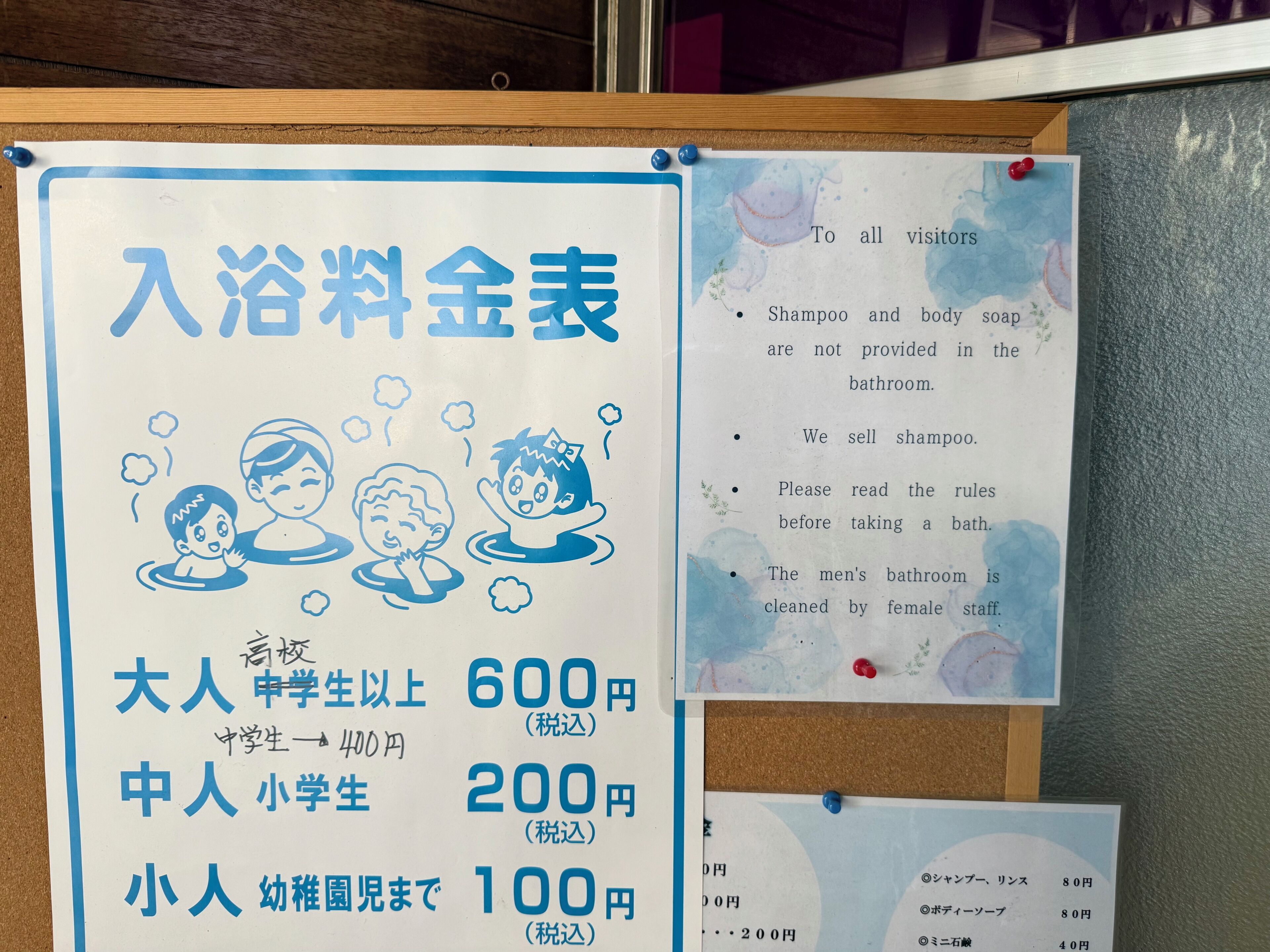 A bulletin board with a sign listing bath fees for different categories of people and a notice about bathroom amenities.