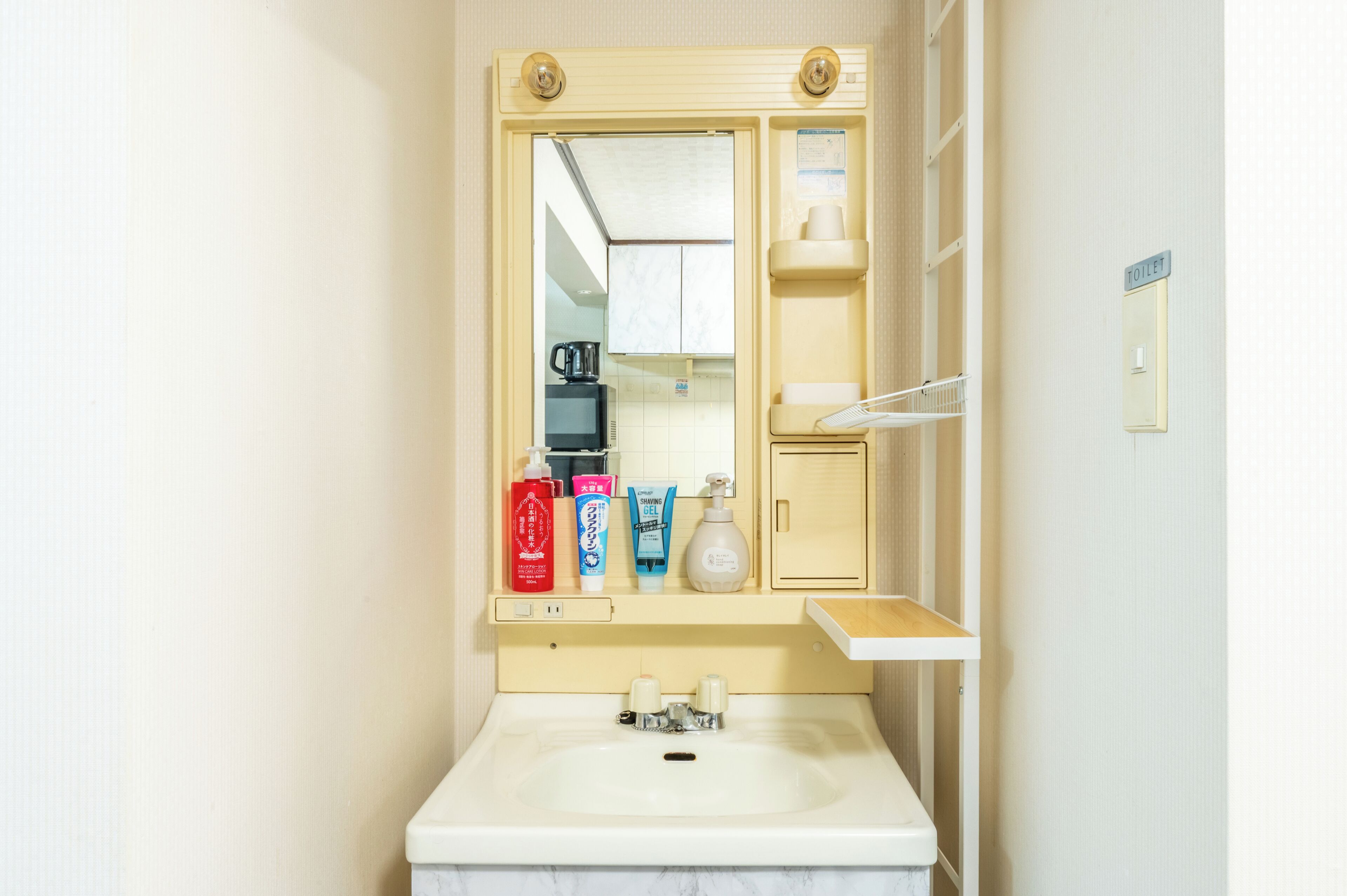 Une salle de bain équipée d’un lavabo, d’un miroir, d’articles de toilette et d’un panneau indiquant les toilettes.