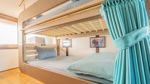 Una cama litera con cortina, suelo de madera y cuadros enmarcados en la pared.