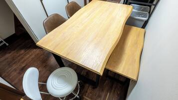 Een houten tafel met vier stoelen, een witte kruk en een zwart metalen rek met plastic bakken.