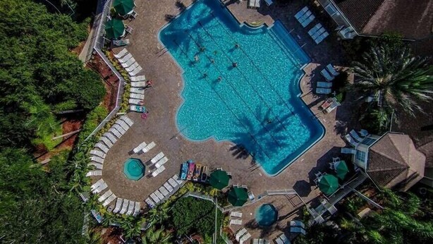 Eine Vogelperspektive eines Resorts mit einem großen rechteckigen Swimmingpool, umgeben von Liegestühlen und Sonnenschirmen.