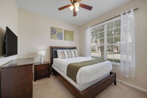 A bedroom with a bed, nightstand, lamp, ceiling fan, artwork, and a window with blinds. - WP2355 - Spacious townhome near all parks (Kissimmee)
