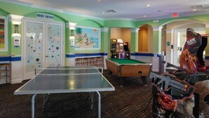 Ein Raum mit Tischtennisplatte, Billardtisch und Spielautomaten.