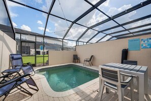 A covered outdoor swimming pool with lounge chairs and a table, surrounded by a glass enclosure. - WP2355 - 3BR Townhome | Resort Access | Near Parks (Kissimmee)