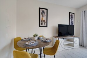 A dining area with a round table, yellow chairs, a TV on a cabinet, and framed pictures on the wall. - WP2355 - 3BR Townhome | Resort Access | Near Parks (Kissimmee)