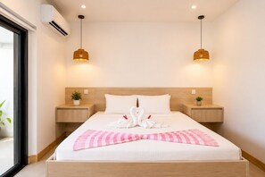 Ein modernes Hotelzimmer mit einem großen Bett, zwei Nachttischen, einer Zimmerpflanze und einem Fenster.