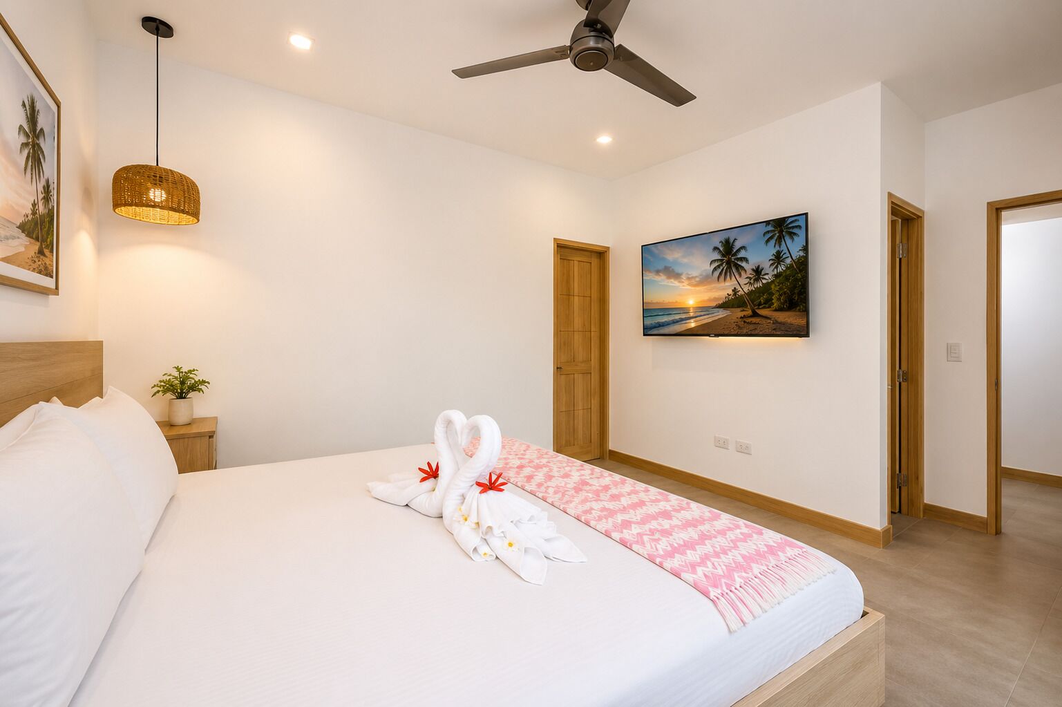 Una habitación de hotel con una cama, un ventilador de techo, un televisor montado en la pared y un cuadro con una playa.