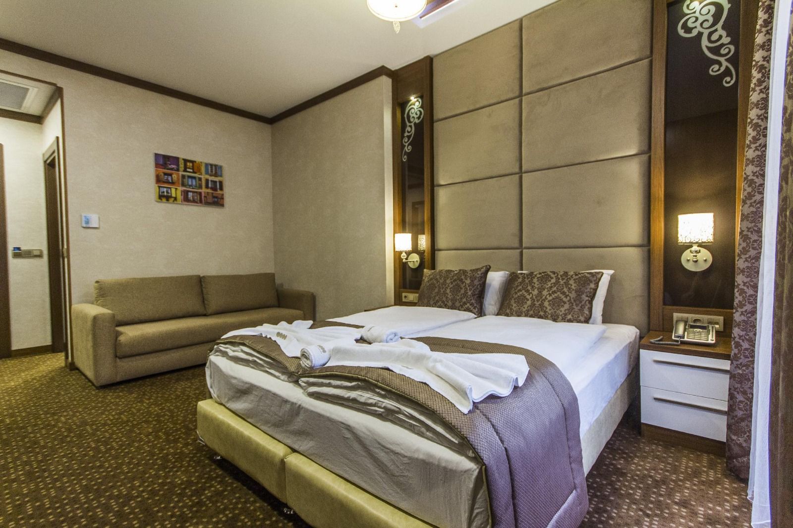 Habitación de hotel con una cama grande, un sofá, una mesita de noche con lámpara y una obra de arte colgada en la pared.