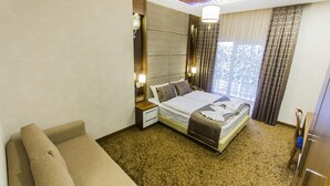 A hotel room with a large bed, a sofa, a nightstand, and a window with curtains.