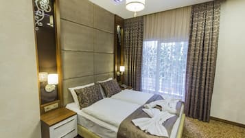 A hotel room with a large bed, a nightstand, a lamp, and a window with curtains.