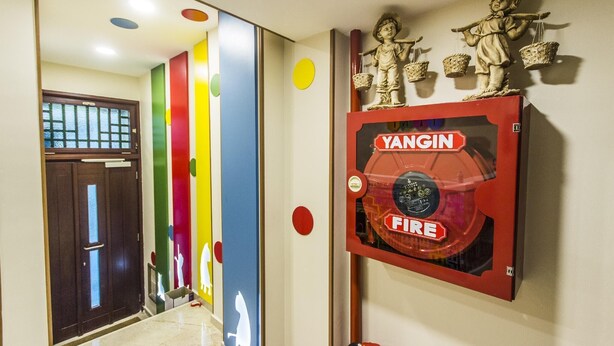 A hallway with a fire alarm box labeled 'YANGIN FIRE' and decorative wall art.
