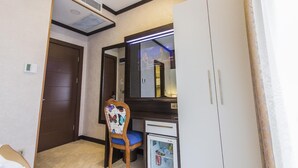A hotel room with a wooden chair, a small desk, a mirror, a wardrobe, and a ceiling vent.