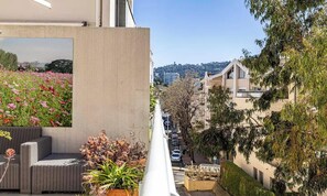 A balcony with wicker furniture, a flower bed, and a view of a city street. - AT A SHORT DISTANCE FROM THE CITY CENTER & THE BEAUTIFUL MEDITERRANEAN BEACHES (Cannes)