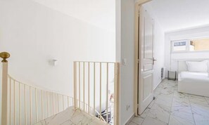 Eine Treppe mit weißer Geländer und einer Tür zu einem Zimmer mit Bett und Heizkörper.