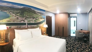 Habitación de hotel con una cama grande, un escritorio, una silla, una lámpara de escritorio, una mesita de noche y un equipo de aire acondicionado instalado en la pared.