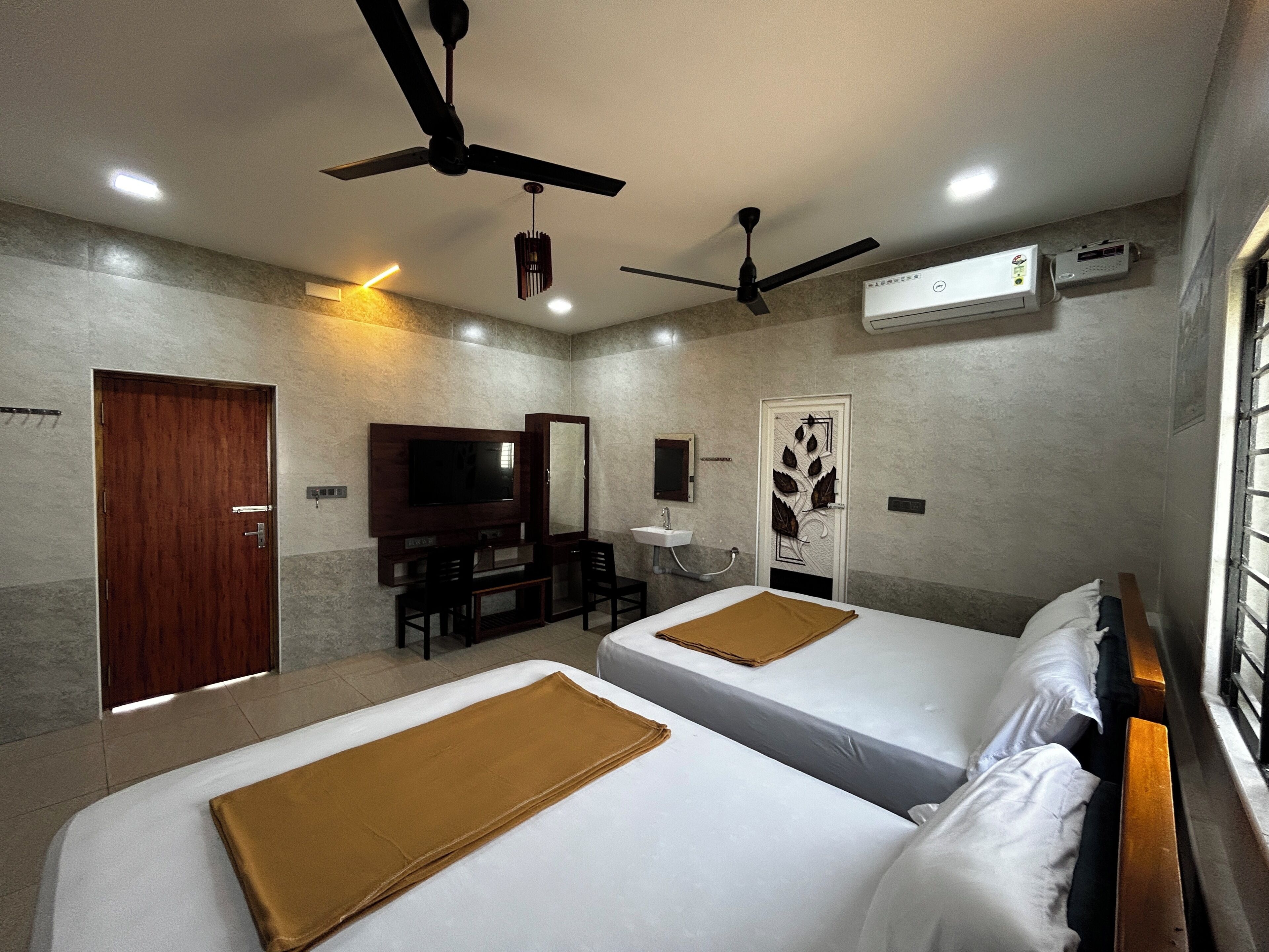 Quarto de hotel com duas camas, televisão, escrivaninha, espelho e ventiladores de teto.