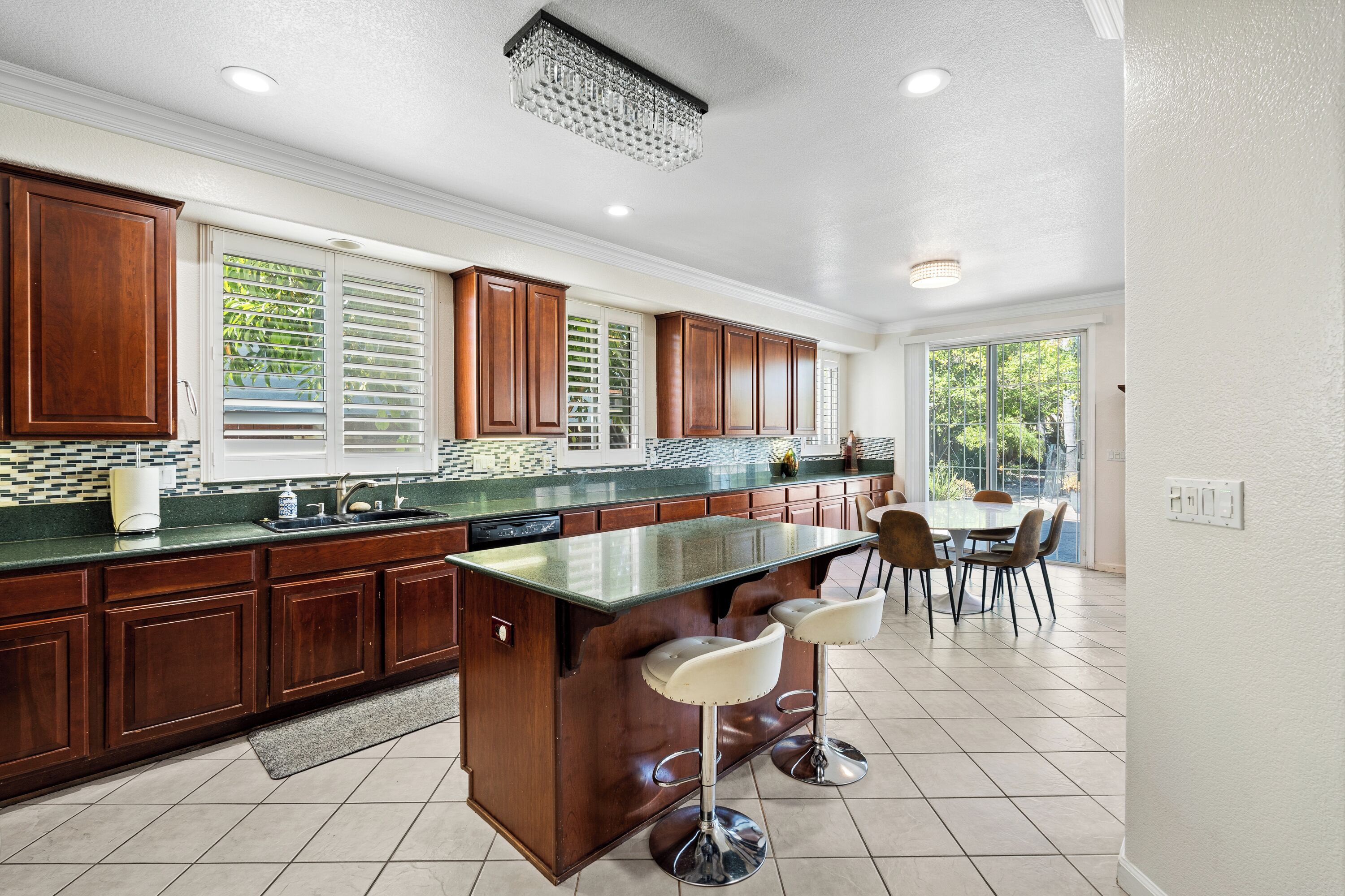 Una cocina con isla central, armarios de madera, salpicadero de azulejos y una zona de comedor con sillas.