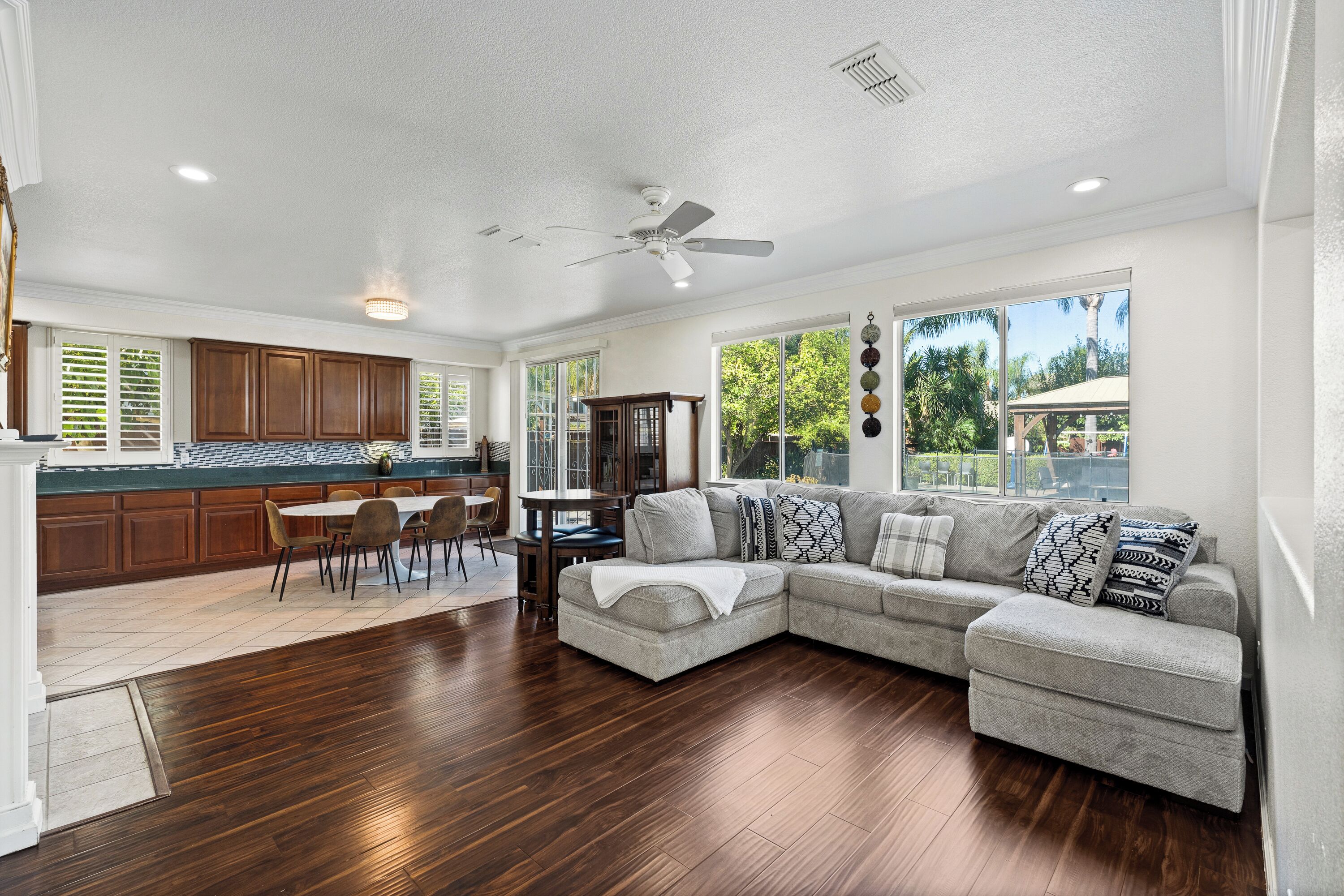 A modern kitchen with dark wood cabinets, a dining area with a round table, and a living room with a large sectional sofa.