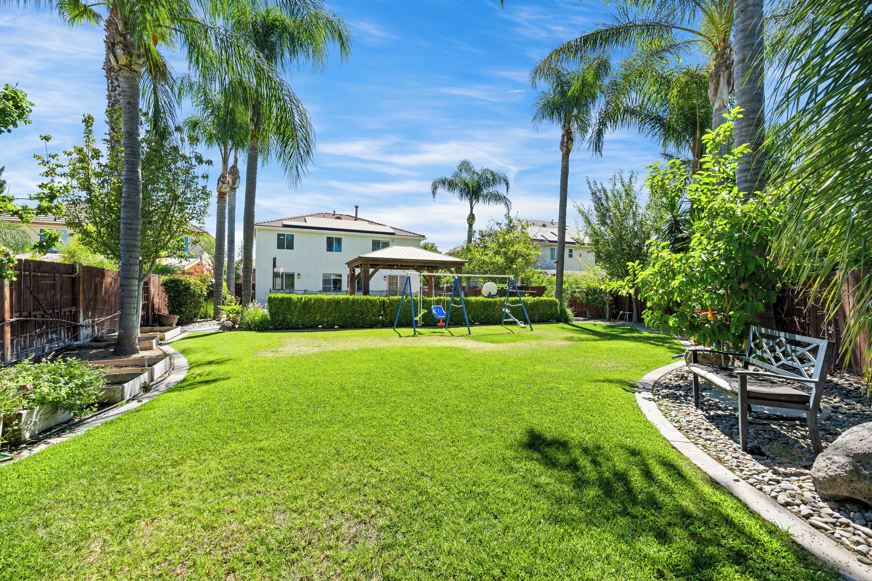 A well-maintained backyard with a lawn, a swing set, and a wooden bench.