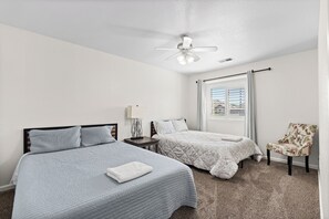Ein Hotelzimmer mit zwei Betten, einem Sessel, einem Deckenventilator und einem Fenster mit Jalousien.