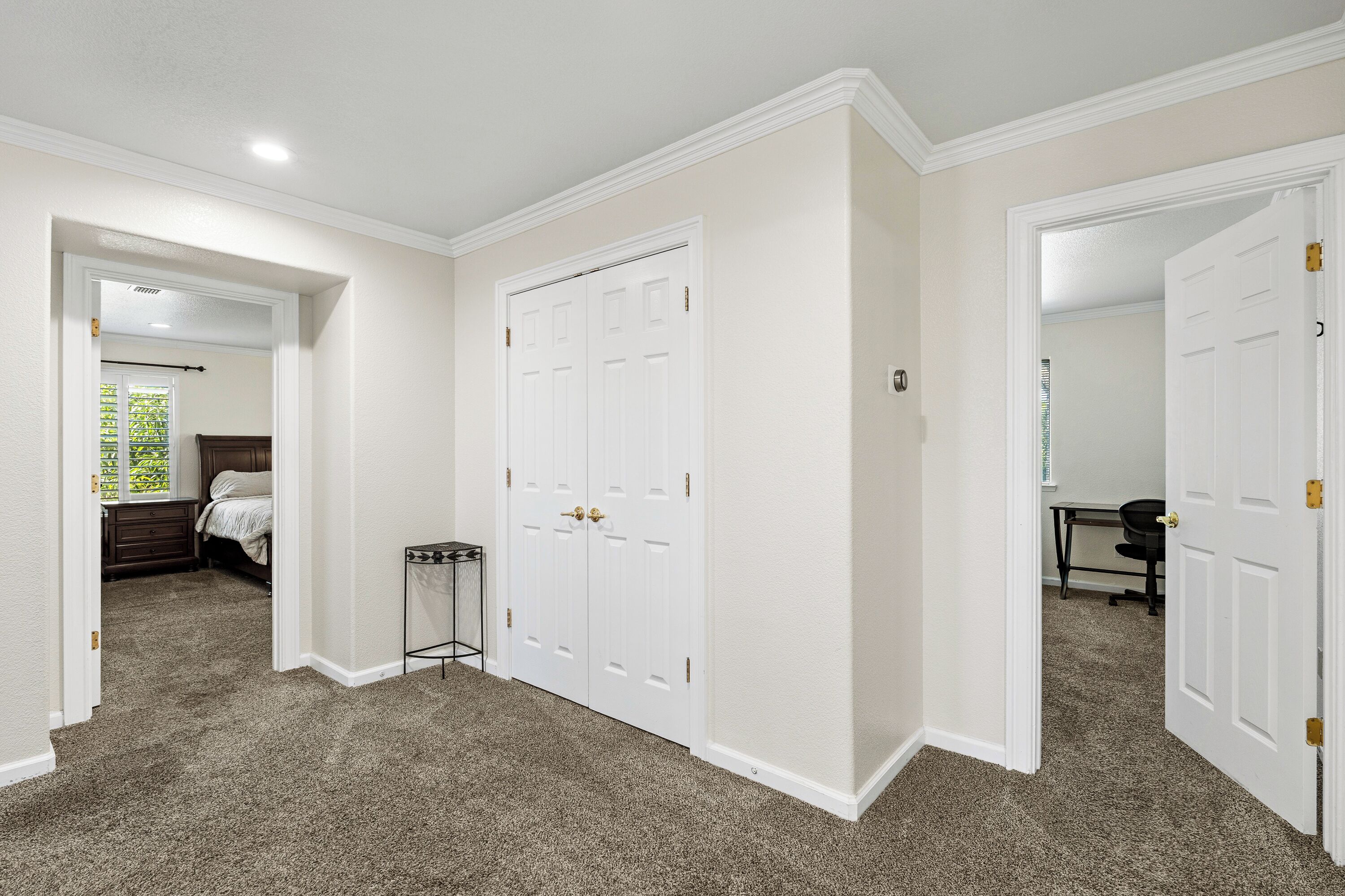 A hallway with carpeted floors, white walls, and double doors with gold handles.