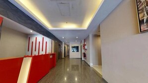 Un pasillo de hotel con un mostrador de recepción rojo, un extintor y un techo con iluminación empotrada.