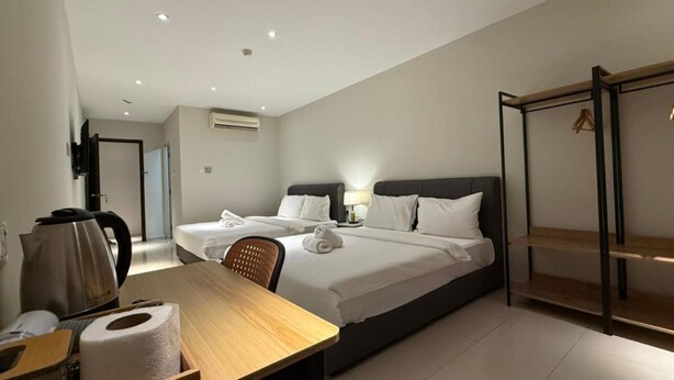 Habitación de hotel con dos camas, un escritorio con hervidor, una silla y un armario con perchero.