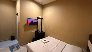 Habitación de hotel con cama, televisión, espejo y una mesita de noche con lámpara.