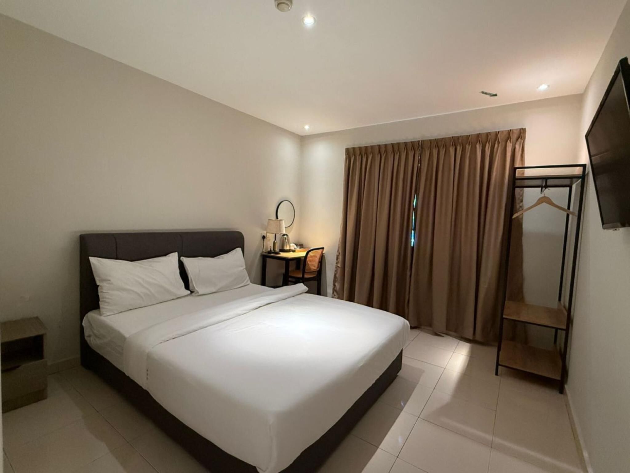Ein Hotelzimmer mit einem großen Bett, einem Nachttisch mit Lampe, einem Kleiderschrank und einem an der Wand befestigten Fernseher.