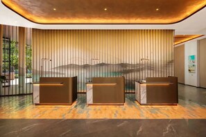 A reception area with three reception desks, a vertical panel with a landscape mural, and a modern ceiling design. - Crowne Plaza by IHG Labuan Bajo (Labuan Bajo)