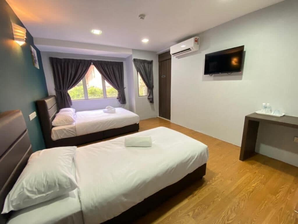 A hotel room with two beds, a desk, a flat-screen TV, and an air conditioning unit.