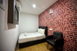 Ein kleines Zimmer mit einem Einzelbett, einem schwarzen Stuhl und einer Wand mit Ziegelmuster.