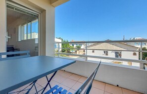 Ein Balkon mit Tisch und Stühlen, der auf ein Wohngebiet mit Häusern und einem klaren Himmel blickt.