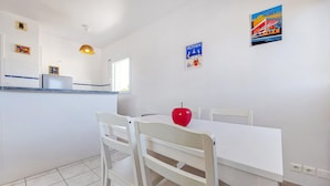 A dining area with a white table and chairs, a red apple on the table, and a poster on the wall. - Charmant appart. proche plage (Royan)
