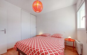 Ein Schlafzimmer mit einem Bett, Kissen, einem Nachttisch, einem Fenster und einer Heizung.