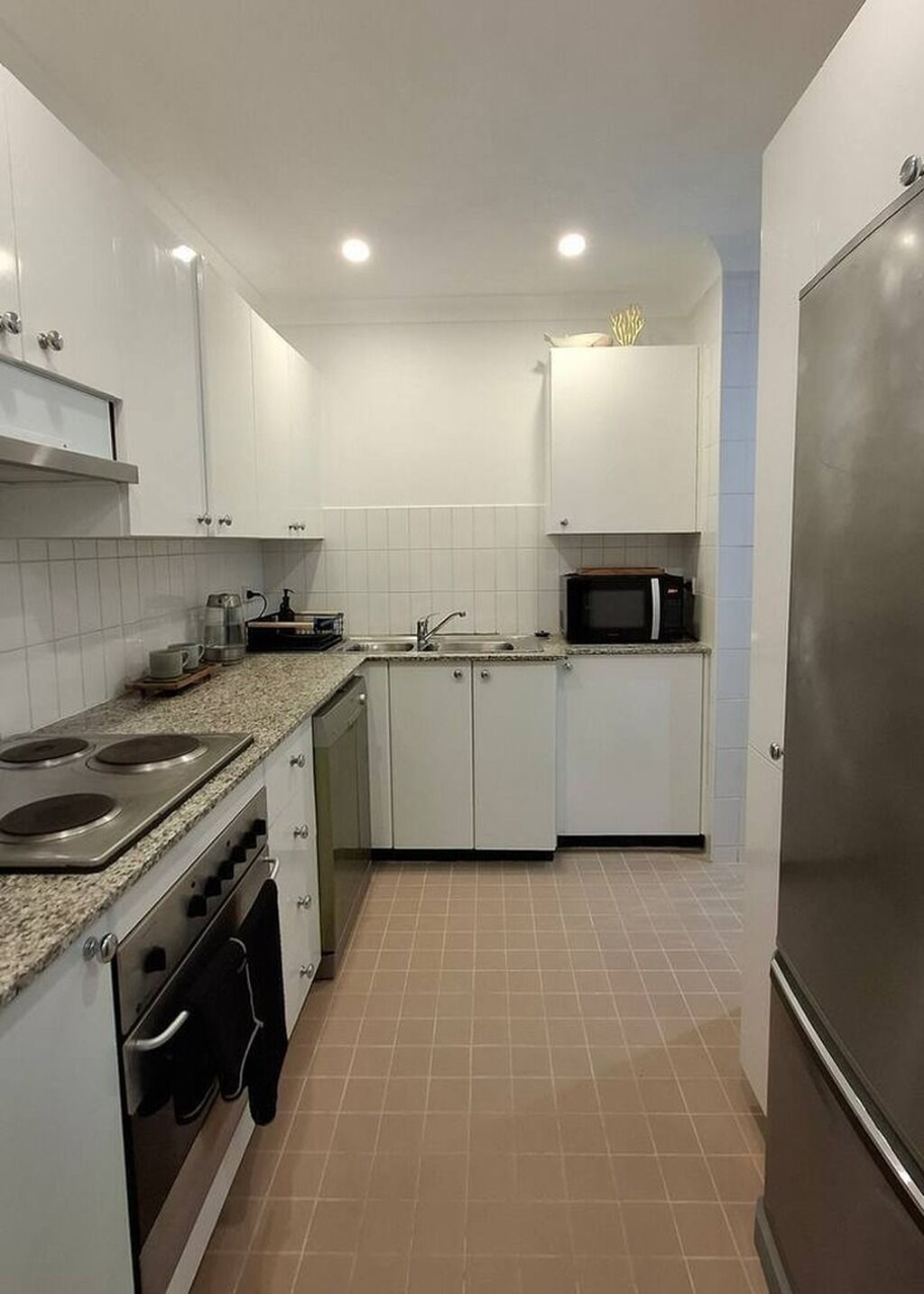 A compact kitchen with white cabinets, a stainless steel refrigerator, a microwave, a stove, and a sink.