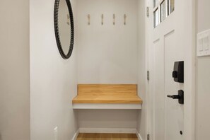 A bathroom with a wooden bench, a white door with a black handle, and a mirror with a black frame. - Pickleball, Pool, Games, Mins to Zilker, SoCo/DT (Austin)