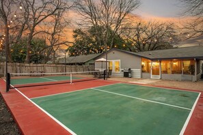 An outdoor tennis court with a net, surrounded by trees and a house with a porch. - Pickleball, Pool, Games, Mins to Zilker, SoCo/DT (Austin)