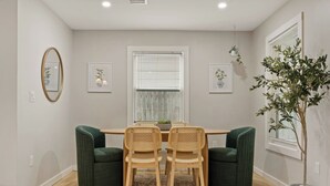 A dining area with a wooden table, two green upholstered chairs, a woven chair, a patterned rug, and a potted plant. - Pickleball, Pool, Games, Mins to Zilker, SoCo/DT (Austin)