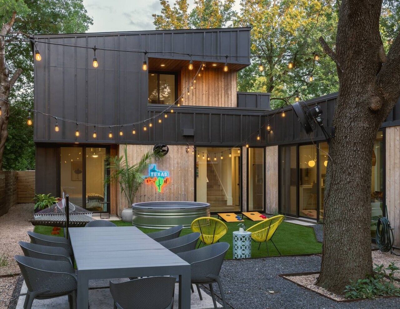 Een modern gebouw met twee verdiepingen, met een patio voorzien van tuinmeubilair en lichtslingers.
