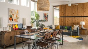Un espacio habitable moderno con comedor, sofá, una planta grande y obras de arte en las paredes.