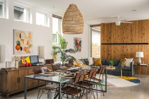 A modern living space with a dining area, a sofa set, a large plant, and artwork on the walls. - Modern Villa | Heated Pool + Movie + 6th St/DT (Austin)