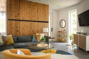 A modern living room with a sofa, armchair, coffee table, and a TV mounted on the wall. - Modern Villa | Heated Pool + Movie + 6th St/DT (Austin)