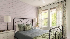 Un dormitorio con cama, mesitas de noche, una ventana con cortinas y un papel tapiz estampado.