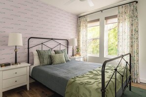A bedroom with a bed, nightstands, a window with curtains, and a patterned wallpaper. - Modern Villa | Heated Pool + Movie + 6th St/DT (Austin)