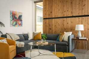 Ein modernes Wohnzimmer mit einem grauen Sofa, einem Glastisch und einer Wand mit Holzverkleidung.
