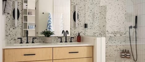 A modern bathroom with a freestanding shower, a wooden vanity with drawers, a mirror, and a small potted plant.