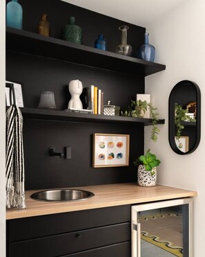 A modern kitchen with black cabinetry, a stainless steel sink, and decorative items on shelves. - Modern Villa | Heated Pool + Movie + 6th St/DT (Austin)